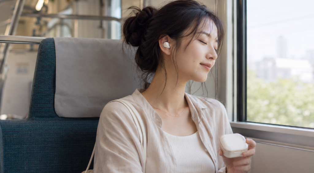 通勤電車でaviot te q3r風の白いワイヤレスイヤホンを装着し、ノイズキャンセリングで音楽を楽しむ日本人女性