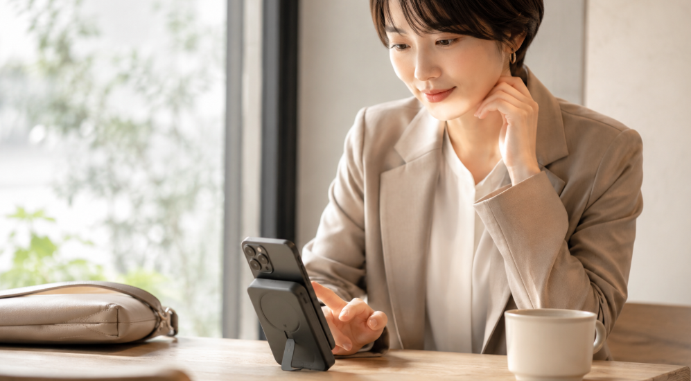 カフェでスマホをMagGo Plusに立てかけてワイヤレス充電する日本人女性