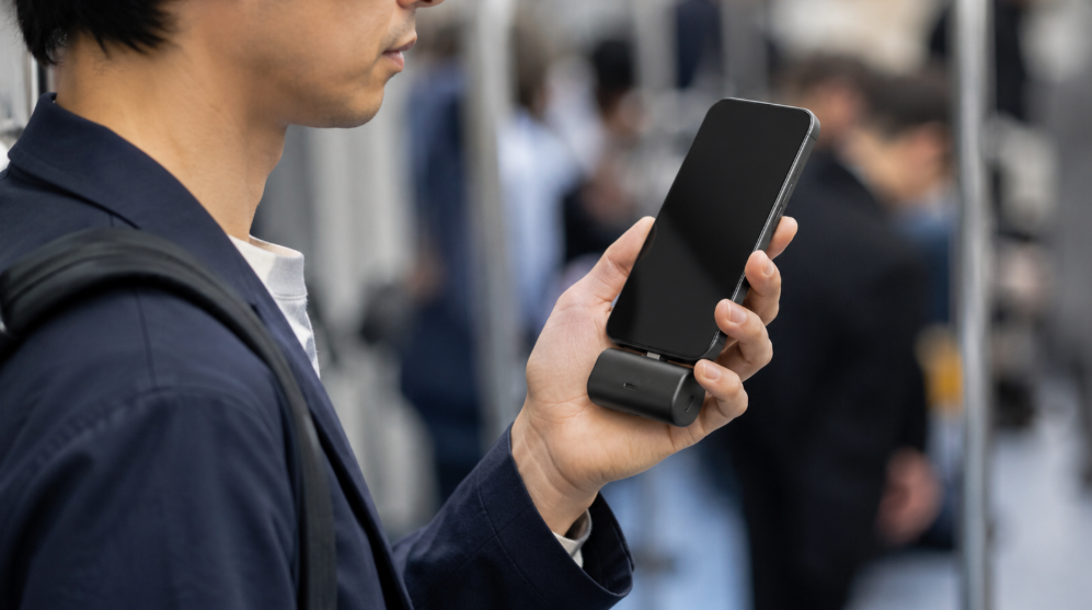 通勤中にUSB-C一体型の小型モバイルバッテリーでスマホを充電する日本人男性