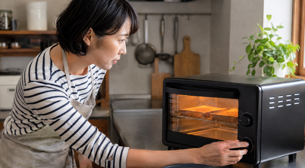 オーブントースターのタイマーを調節しながらパンの焼き加減を確認する様子