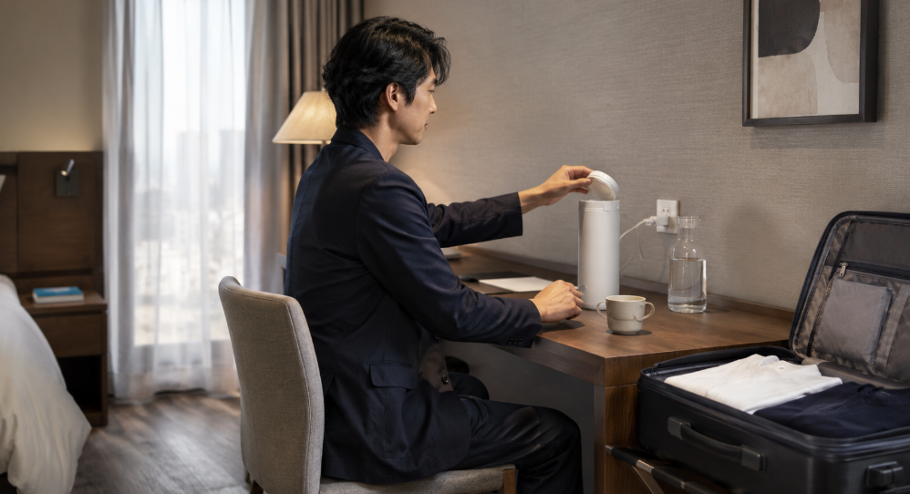 国内ホテルでECLEAR ポータブルケトルを使う日本人男性と旅行用スーツケース